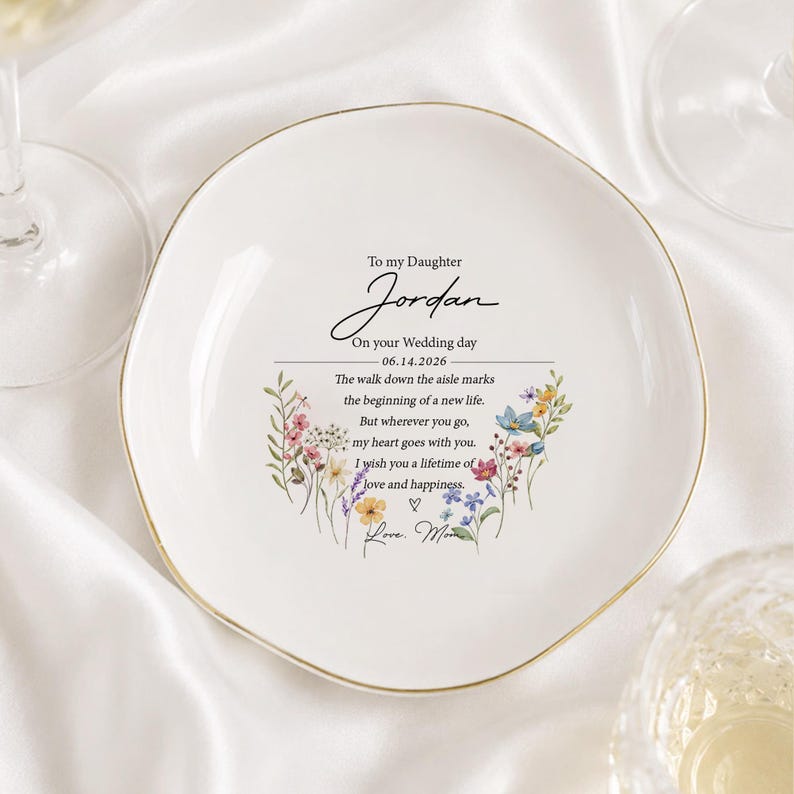 May include: A white ceramic trinket dish with an irregular, organic shape and a gold-painted rim. The center features black text reading To my Daughter Jordan On your Wedding day 06.14.2026, surrounded by a colorful floral illustration and a message.