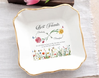 May include: A white ceramic mug with a black handle and the text "But First, Coffee" in a bold, black font. The mug is set against a blurred background, suggesting a cozy setting.