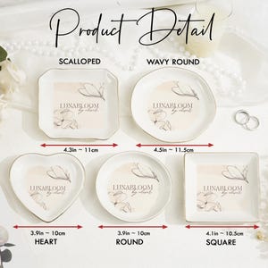 May include: Five white ceramic trinket dishes in scalloped, wavy round, heart, round, and square shapes. Each dish features a floral line art graphic and the text LUNABLOOM by oliver. Dimensions range from 3.9 inches to 4.5 inches in width.