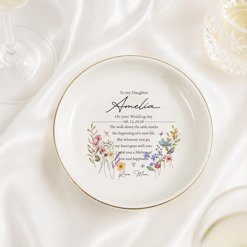 May include: A round white ceramic trinket dish with a gold-trimmed edge. The center features a floral wreath design surrounding the text: To my Daughter Amelia, On your Wedding day 06.14.2026, The walk down the aisle marks the beginning of a new life.