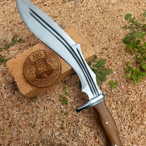 May include: A large, silver-bladed knife with three black stripes on the blade and a wooden handle. The handle is a dark brown color with a silver bolster. A wooden coaster with the text "HG NORTHCRAFT" is visible.