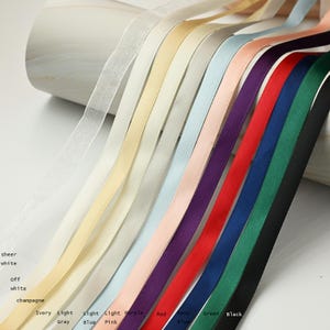 May include: A collection of colorful ribbons in various shades, including sheer white, ivory, light gray, light blue, light pink, purple, red, navy blue, green, and black. The ribbons are arranged in a diagonal pattern, showcasing their different colors and textures.