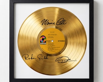 May include: Framed gold record featuring the "Best of Bee Gees" album. The record has signatures and a yellow label with song titles. The frame is black, and the record is displayed on a white background.