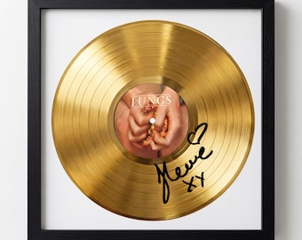May include: A framed gold record with a black frame. The record has a center label with the word "LUNGS" and an image of hands. The record is signed in black ink with a heart symbol and the name "Heve" and "XX".