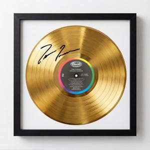 May include: Framed gold record of Tina Turner's "Private Dancer" album. The record is gold-colored with a black signature and a colorful label. The record is displayed in a black frame, creating a striking contrast.