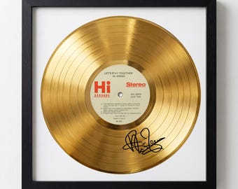 May include: A framed gold record of Al Green's "Let's Stay Together" album. The record has a gold finish and features the Hi Records label. The album title and artist's name are visible, along with a signature. The frame is black.