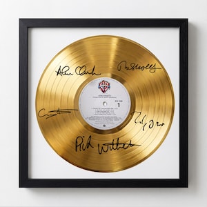 May include: A framed, gold-colored vinyl record with signatures. The record's label features the band name, "Dire Straits," and song titles. The frame is black, and the record is centered on a white background.