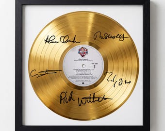 May include: A framed, gold-colored vinyl record with signatures. The record's label features the band name, "Dire Straits," and song titles. The frame is black, and the record is centered on a white background.
