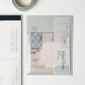 May include: A clear plastic package containing tracing paper sticky notes. The package has a light green border and contains various patterned paper pieces. A roll of washi tape is in the upper left corner. Text on the package reads "ORIGINAL STATIONERY TRACINGPAPER STICKY NOTES".