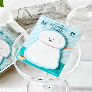 May include: A pack of "Katanuki Fusen" sticky notes with a white dog design, light blue border and background. The package contains 20 sheets. The notes are displayed in a clear glass bowl.