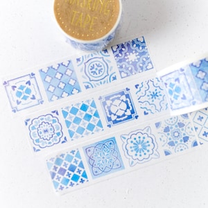Puede incluir: Cinta adhesiva decorativa con un patrón repetitivo de diseños de azulejos azules y blancos. El rollo de cinta es visible en la parte superior, con las palabras "MASKING TAPE" impresas. Ideal para scrapbooking, manualidades y proyectos decorativos.