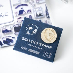 May include: A navy blue sealing stamp set with a gold-colored stamp and a matching navy blue card. The card has the words "SEALING STAMP" and "...Fountain pen..." printed on it, along with the text "eric design" and "NICE DAY!"