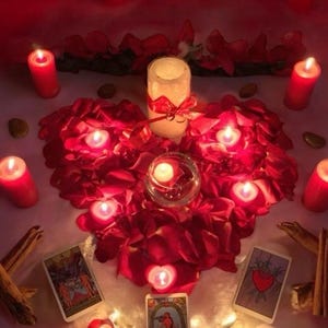 May include: A romantic scene with lit candles and red rose petals arranged in a heart shape. A large pillar candle is tied with a red ribbon. Tarot cards and cinnamon sticks are also present, creating a mystical ambiance.
