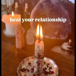 May include: Two white taper candles bound together with twine, decorated with dried flower petals, and placed on a silver-toned scalloped plate. The candles are lit, and the text "heal your relationship" is centered in the image.
