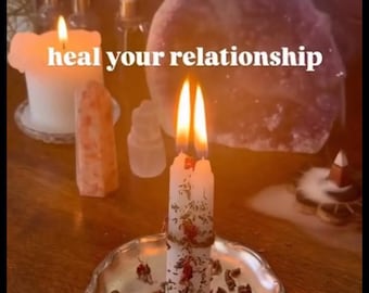 May include: Two white taper candles bound together with twine, decorated with dried flower petals, and placed on a silver-toned scalloped plate. The candles are lit, and the text "heal your relationship" is centered in the image.