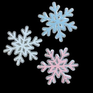 May include: Three snowflake-shaped patches featuring a glossy, raised texture. One snowflake is light blue, one is white, and one is light pink. Each snowflake has a distinct six-pointed crystalline structure with intricate, symmetrical branch details.