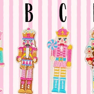May include: Four embroidered nutcracker patches labeled A, B, C, and D. Patch A holds a candy cane, B has a mustache, C holds a lollipop, and D features a gingerbread-inspired design. Each figure displays vibrant pink, blue, and gold thread.