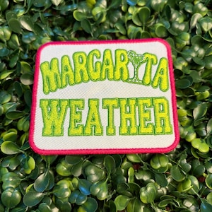 May include: A square patch with the words "Margarita Weather" in green, outlined in yellow, on a white background. The patch has a pink border and a green cocktail graphic. The patch is set against a background of green leaves.