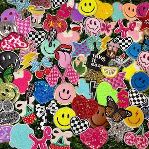 May include: A collection of colorful, embroidered patches with various designs, including smiley faces, hearts, stars, and flags. Some patches feature glitter, sequins, and beaded details. The patches are in a variety of colors, such as pink, yellow, blue, and black.