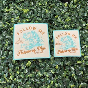 May include: Two square patches with the text "FOLLOW ME" and "Fishers of Men" in a stylized font. The patches feature a teal fish illustration. The patches are on a green leafy background.