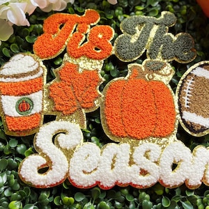 May include: A multi-piece chenille patch set featuring the text 'Tis The Season' in orange and dark green. The design includes a coffee cup with whipped cream, an orange maple leaf, a large orange pumpkin, and a brown football with white laces.