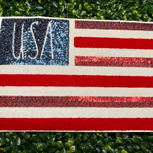 May include: A rectangular decorative piece featuring the American flag design. The upper left corner has a blue sequined field with the word "USA" in white. The flag has red and white stripes.