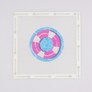 May include: A square needlepoint canvas featuring a circular life preserver design in the center. The life preserver has alternating pink and white segments with a blue water-like pattern in the middle. The text AB NEEDLEPOINT is printed on the border.