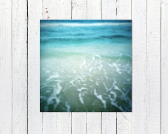 May include: A blurry photograph of a turquoise ocean with white foamy waves crashing on the shore.