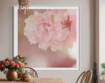 May include: A framed print of a close-up of pink cherry blossoms with a soft, blurred background. The print is hanging on a wall in a room with a wooden table and chairs.