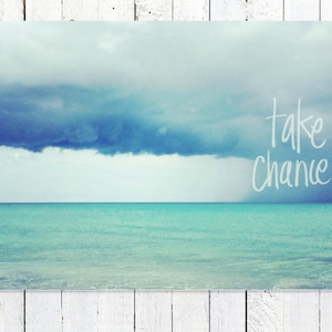 May include: A photograph of a turquoise ocean with a dark blue cloud in the sky. The text "take chances" is written in white on the image.