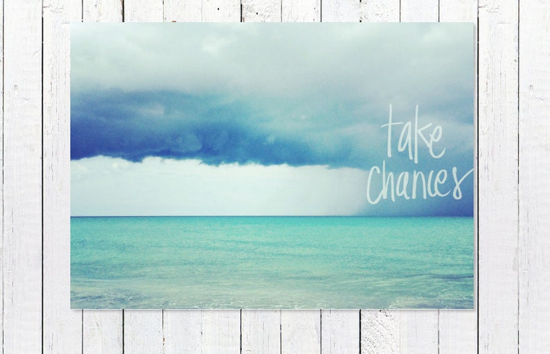 May include: A photograph of a turquoise ocean with a dark blue cloud in the sky. The text "take chances" is written in white on the image.
