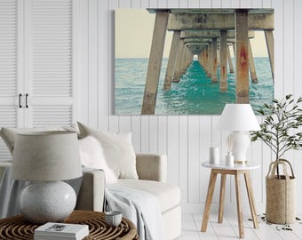 May include: A living room interior with a white couch, a wicker coffee table, a side table with a lamp, and a framed photograph of a pier over turquoise water.