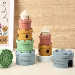 Könnte beinhalten: Stapelturm-Spielzeug-Set in Pastellfarben. Das Set enthält eine hellgrüne Basis mit dem Namen "Amelia" und weitere Teile in Gelb, Rosa und Blau. Der Turm ist mit einem weißen, kegelförmigen Dach versehen. Das Set ist für Kinder konzipiert.