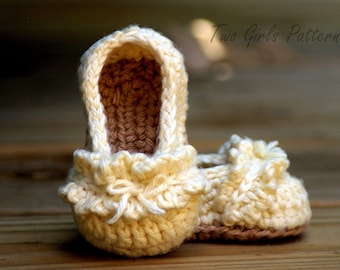 Könnte beinhalten: Ein Paar gehäkelte Babyschuhe in Cremefarbe mit einem Rüschenbesatz. Die Schuhe sind aus weichem Garn gefertigt und haben einen zarten, femininen Look.