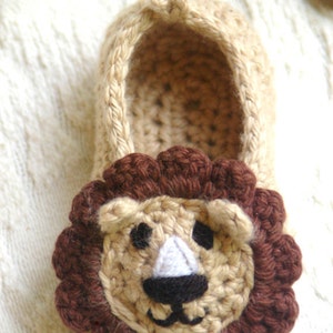 May include: Crocheted lion slippers in beige and brown. The slippers have a brown mane and a cute lion face with black eyes and a white nose.