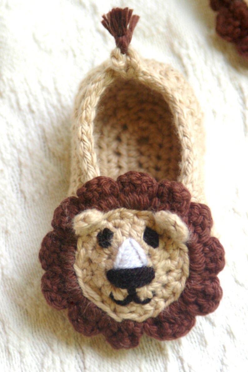 May include: Crocheted lion slippers in beige and brown. The slippers have a brown mane and a cute lion face with black eyes and a white nose.