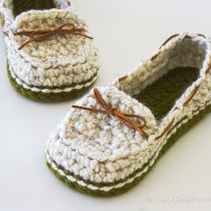 May include: A pair of crocheted slippers in white with a green trim and brown leather laces. The slippers have a casual loafer style.
