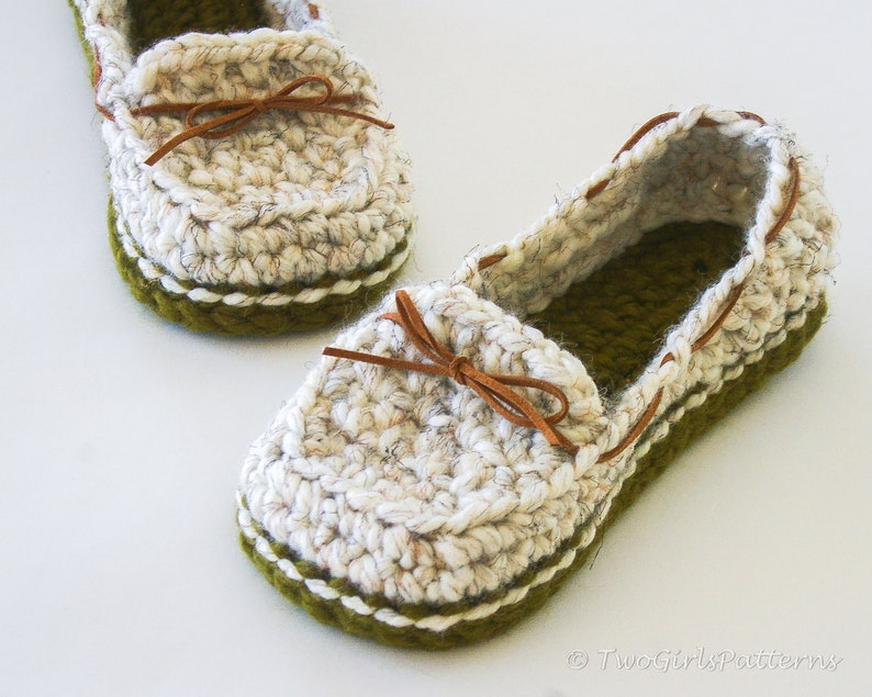 May include: A pair of crocheted slippers in white with a green trim and brown leather laces. The slippers have a casual loafer style.
