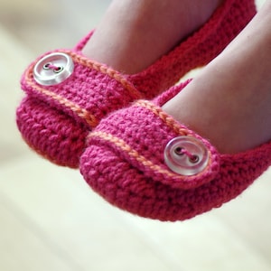 May include: A pair of pink crocheted baby shoes with orange trim and white buttons.