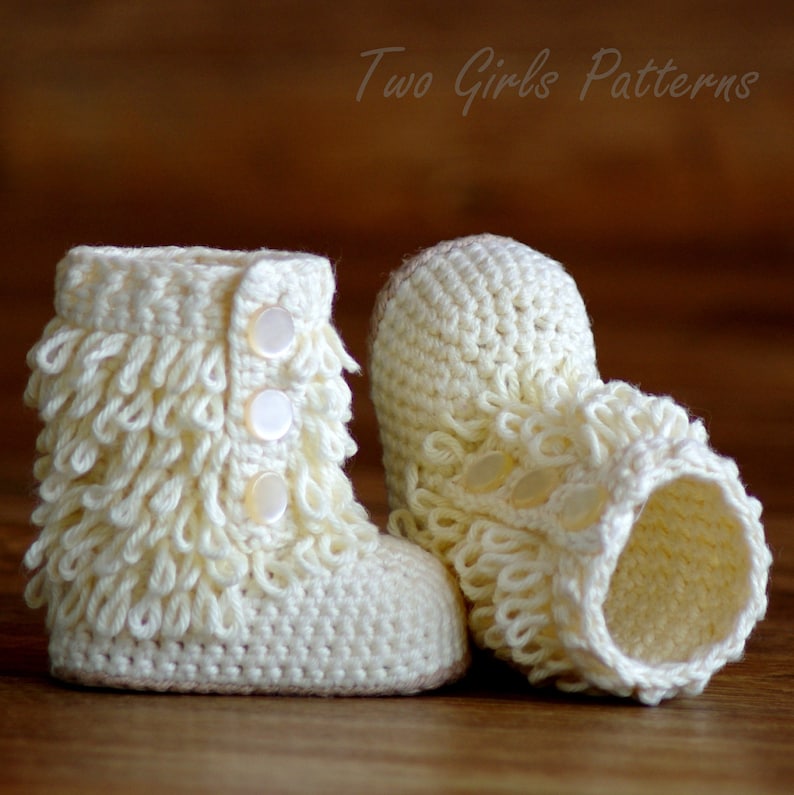 Puede incluir: Un par de botitas de beb&eacute; de ganchillo blanco con un borde de volantes y detalles de botones. Las botitas est&aacute;n sobre una superficie de madera.
