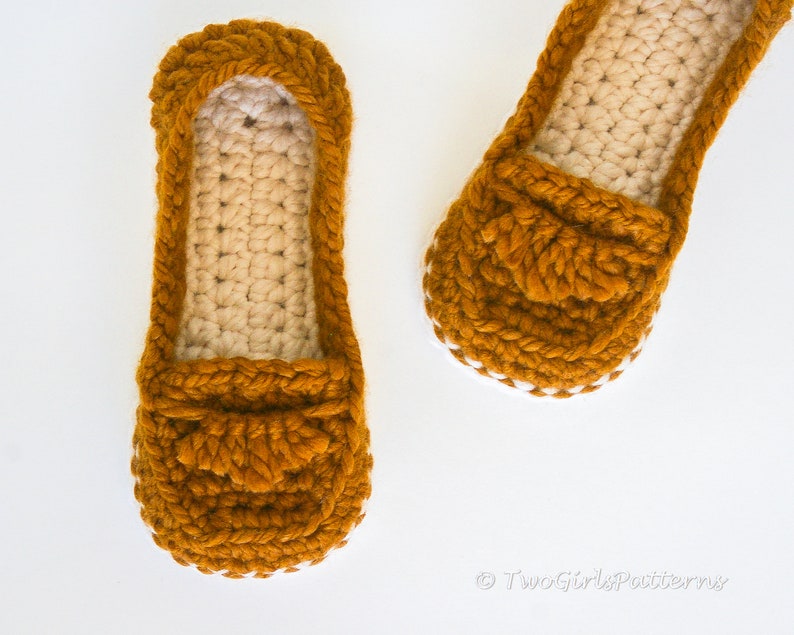 May include: A pair of crocheted slippers in a mustard yellow color with a white crocheted trim. The slippers have a loafer style with a crocheted detail on the top.