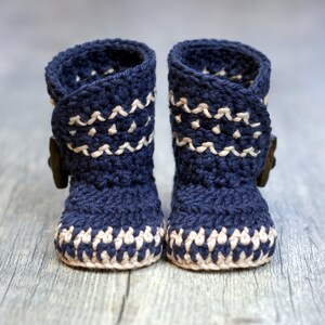 K&ouml;nnte beinhalten: Ein Paar marineblaue geh&auml;kelte Babyschuhe mit wei&szlig;em Besatz und einem Knopfdetail.