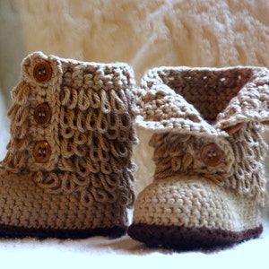 Puede incluir: Un par de botines de beb&eacute; de ganchillo beige con ribetes marrones y botones marrones.