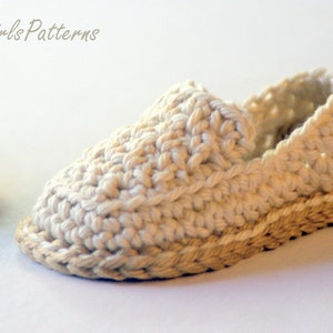 May include: A pair of crocheted baby shoes with a beige sole. The shoes are made with a white yarn and have a simple design.