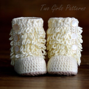 May include: A pair of white crocheted baby booties with a ruffled trim and white buttons. The booties have a light brown sole.