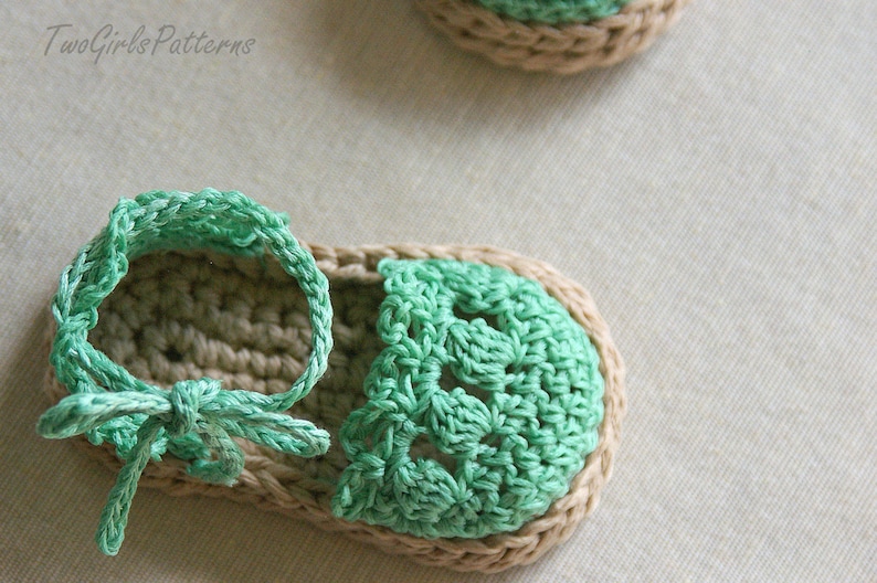May include: A pair of crocheted sandals with a green and beige color scheme. The sandals have a simple design with a single strap that wraps around the ankle.