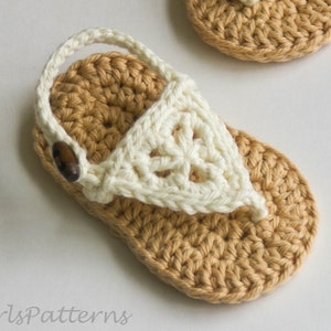 Peut inclure: Sandale de bébé au crochet faite à la main, de couleur beige et crème. La sandale présente une semelle beige, une bride crème et une fermeture à bouton en bois. La sandale mesure environ 10 cm de long.