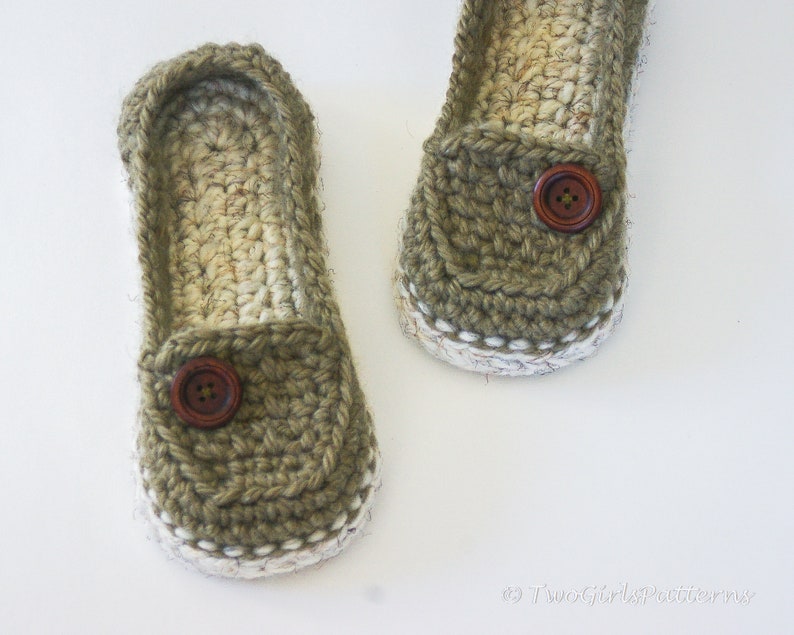 May include: A pair of crocheted slippers with a brown button on each. The slippers are made with a white and green yarn.