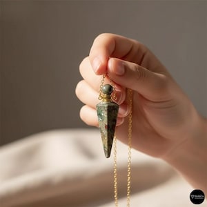 Op de afbeelding: Een groene en rode stenen hanger met een goudkleurige ketting. De hanger heeft de vorm van een fles met een puntige onderkant en een afgeronde bovenkant. De fijne ketting hangt aan de bovenkant van de hanger.