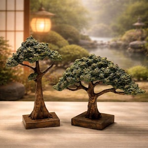 May include: Two miniature bonsai trees with textured green foliage and brown trunks sit on square wooden bases. The trees are displayed on a light-colored wooden surface, with a blurred outdoor scene in the background.